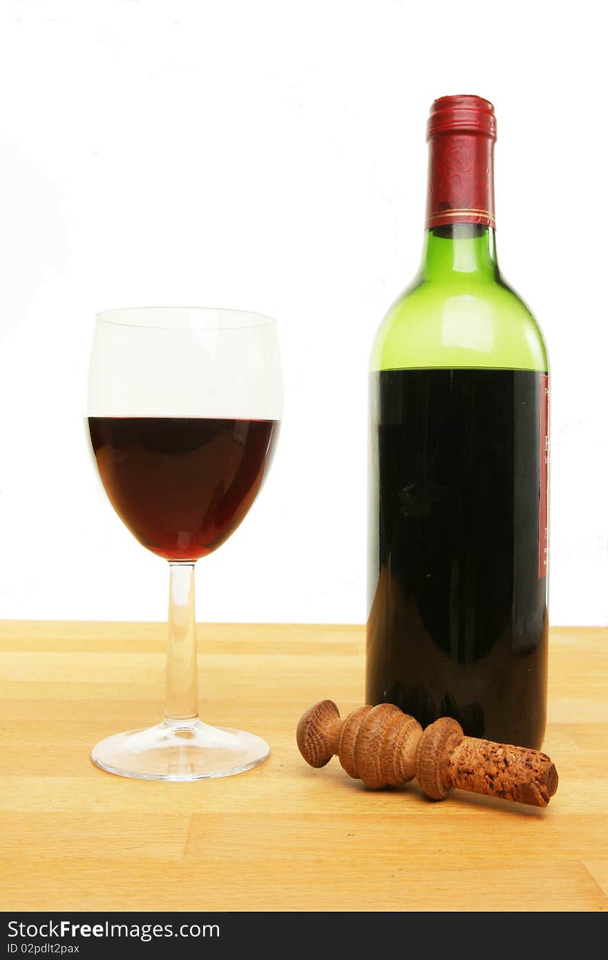 Glass and bottle of red wine with a stopper on wood