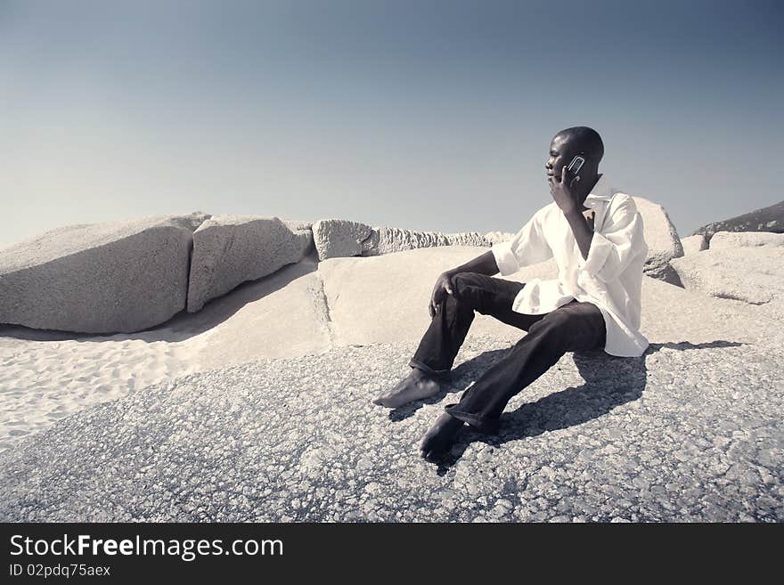 Black man sitting on a beach and using a mobile phone. Black man sitting on a beach and using a mobile phone