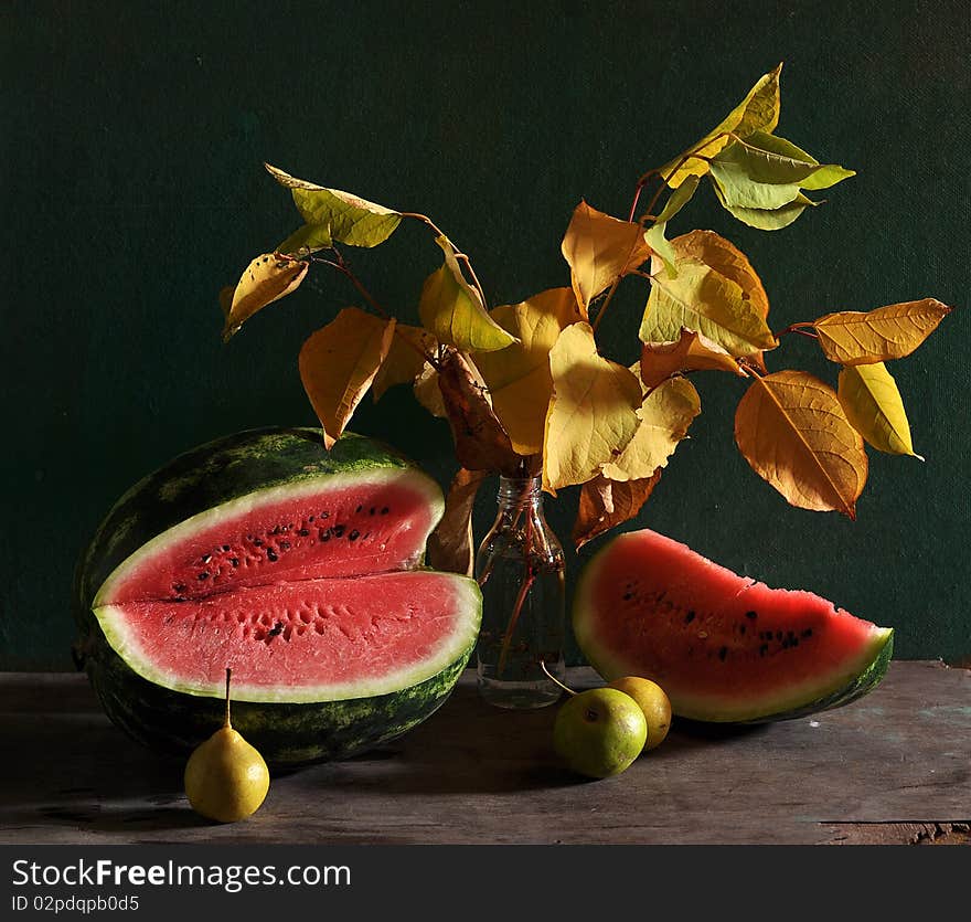 On a table cost yellow leaves in a glass bottle, alongside pears and cut water-melon lie on a table. On a table cost yellow leaves in a glass bottle, alongside pears and cut water-melon lie on a table.