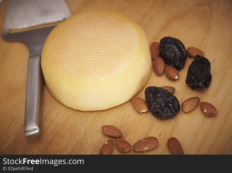 Cheese round with almonds and prunes on a wooden board.