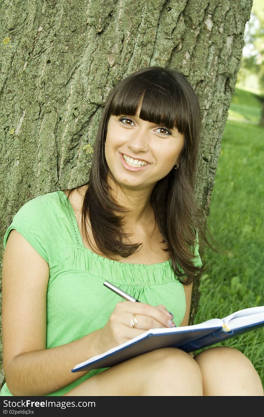 Young beautiful woman in a park with a notebook and pen. Thought of writing. Young beautiful woman in a park with a notebook and pen. Thought of writing