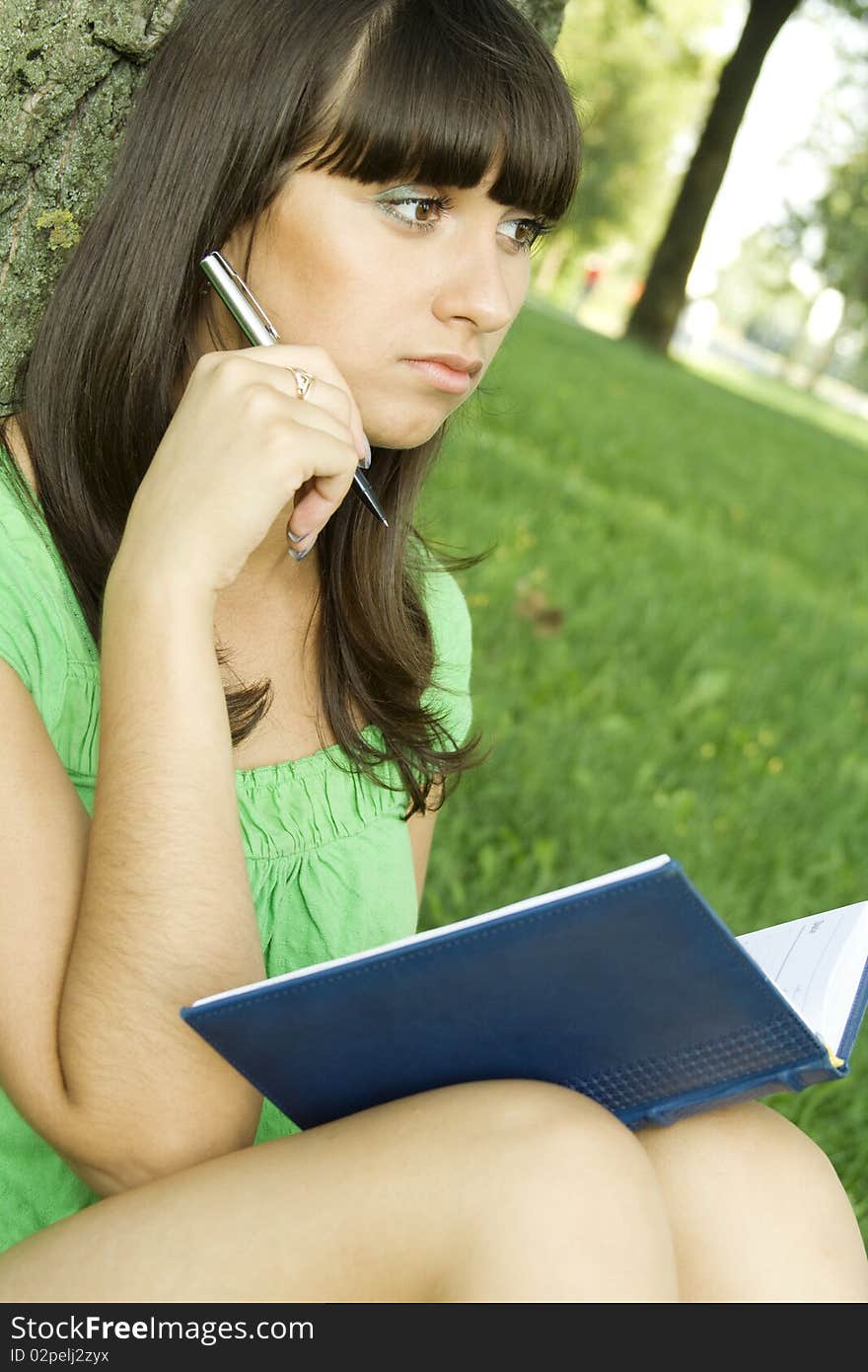 Young beautiful woman in a park with a notebook and pen. Thought of writing. Young beautiful woman in a park with a notebook and pen. Thought of writing