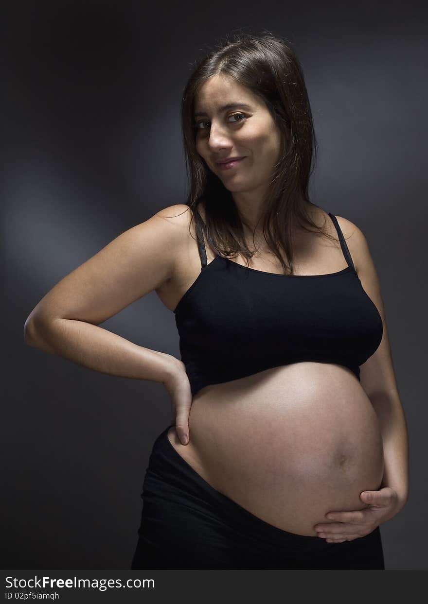 Pregnant woman holding her belly over a gray background.