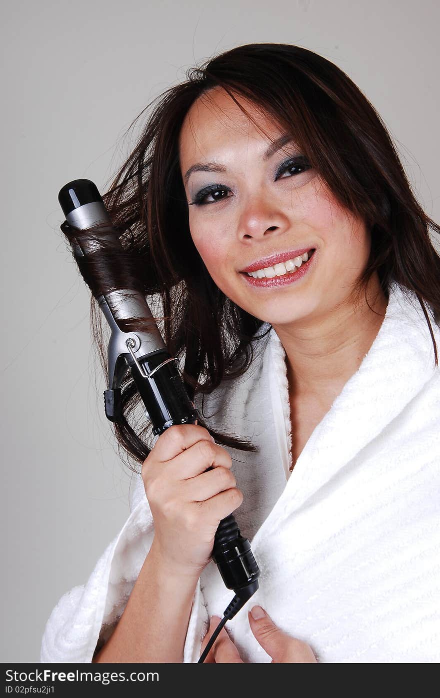 A pretty Chinese woman, is curling her hair, dressed in a white bath robe
for light gray background. A pretty Chinese woman, is curling her hair, dressed in a white bath robe
for light gray background.