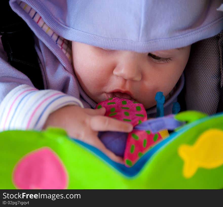 Baby girl sitting in the stroller and plays toys