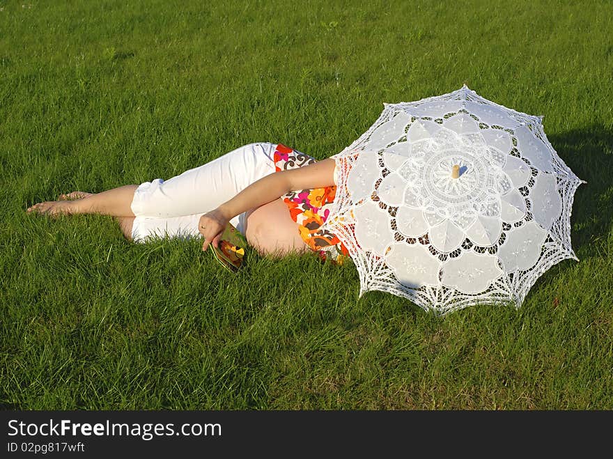 Pregnant woman lying on the grass, reading the small book