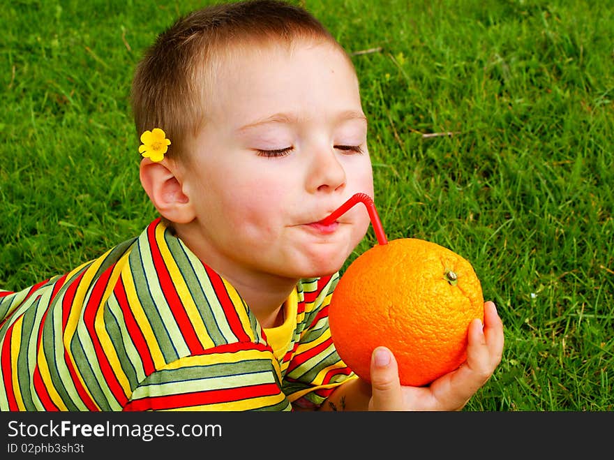 The child is drinking orange juice through a tube inserted in an orange background grass