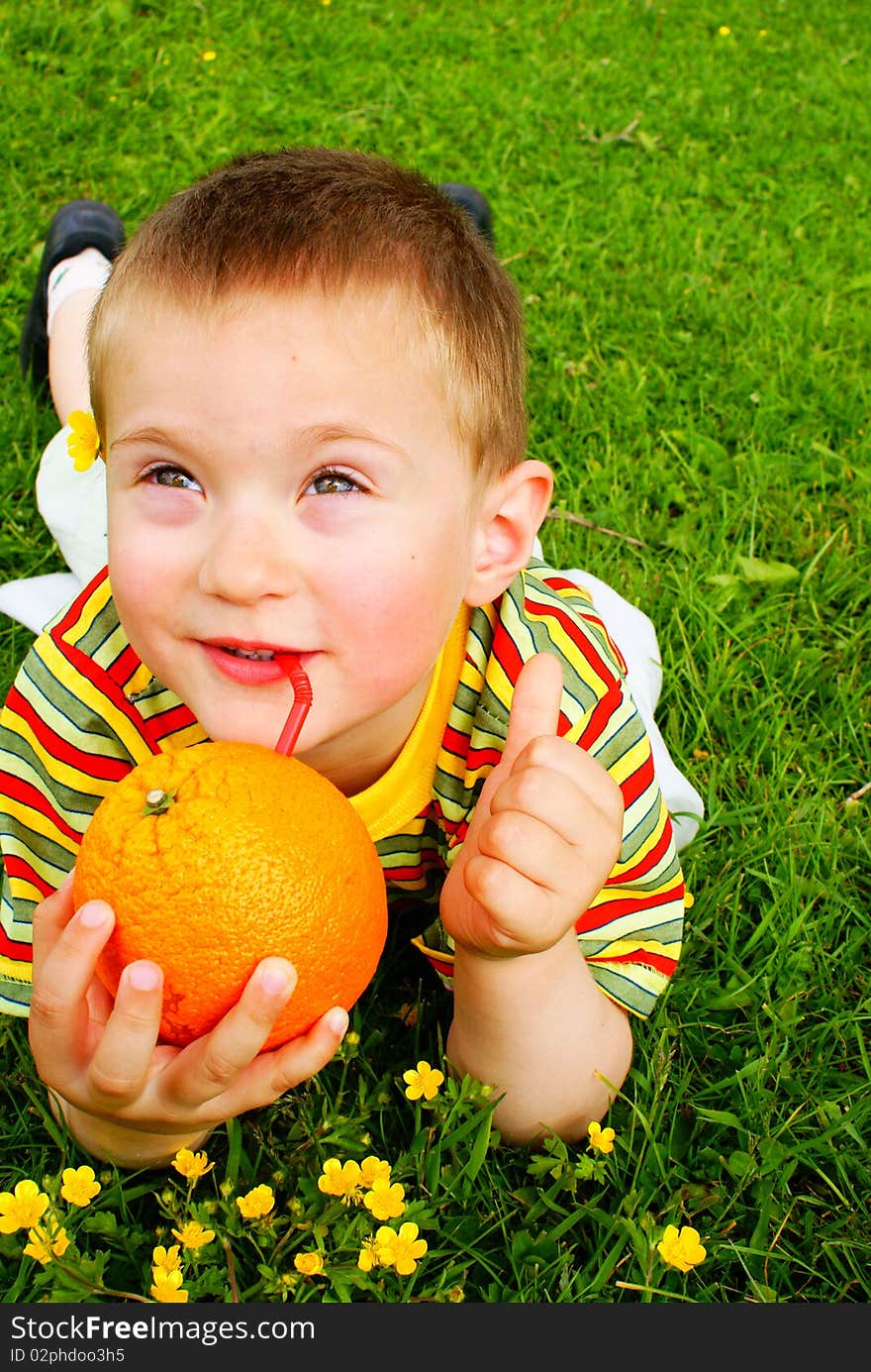 The child is drinking orange juice through a tube inserted in an orange background grass