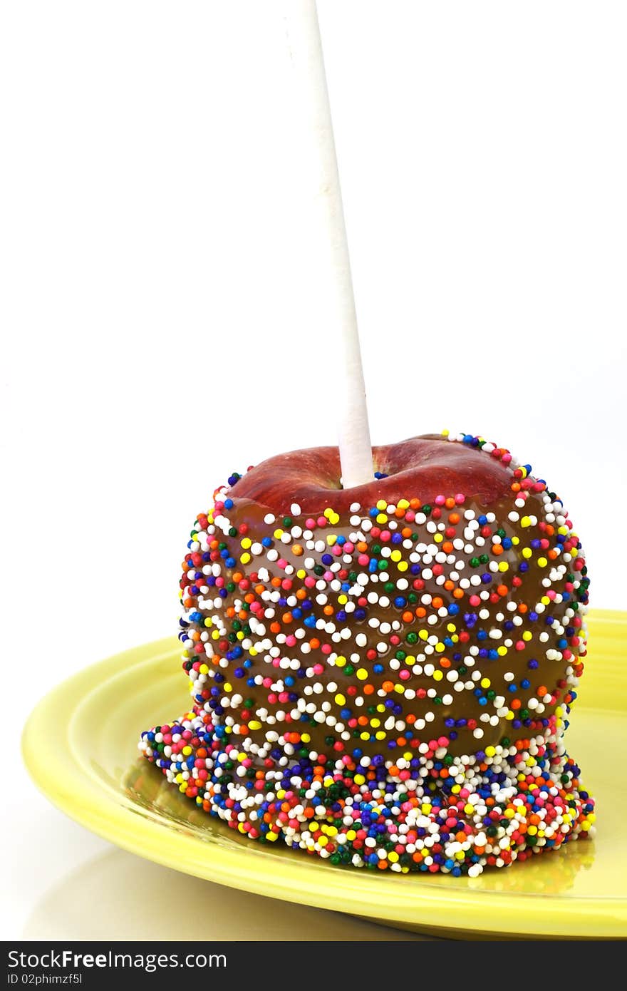 Closeup of caramel apple with rainbow sprinkles on a yellow plate over an isolated white background