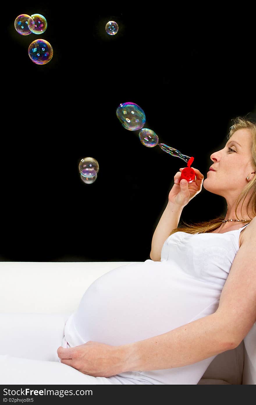 Young fresh pregnant woman with blow bubbles  sitting on a couch over black background. Young fresh pregnant woman with blow bubbles  sitting on a couch over black background.