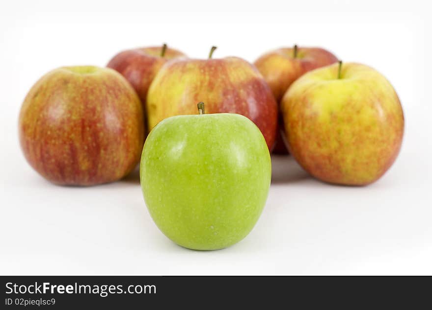 One green apple in front of red apples