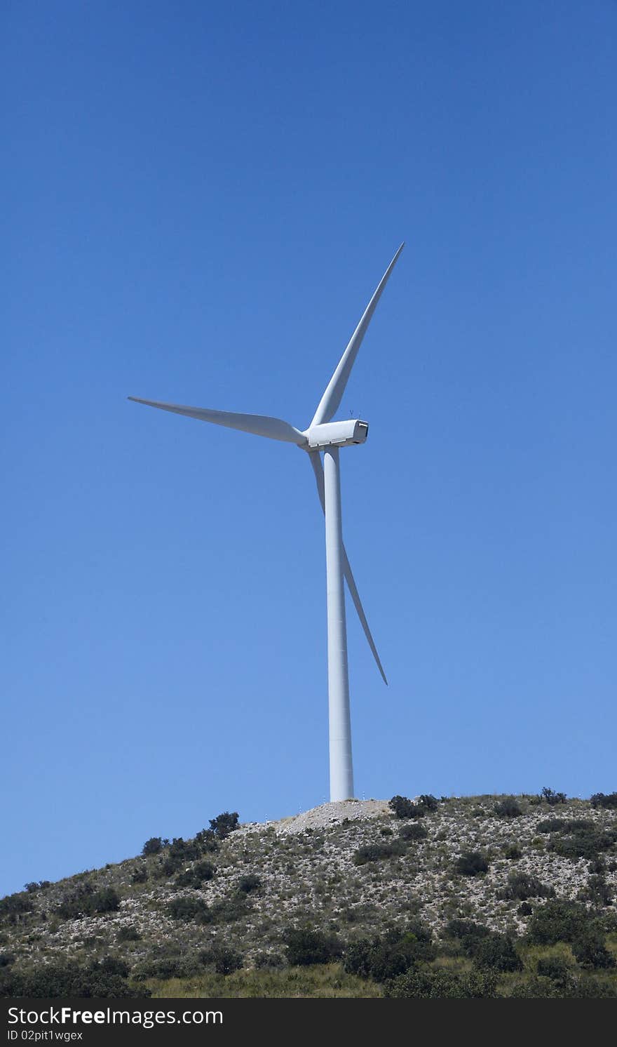 A Wind Turbine on a hilltop with clear blue sky.