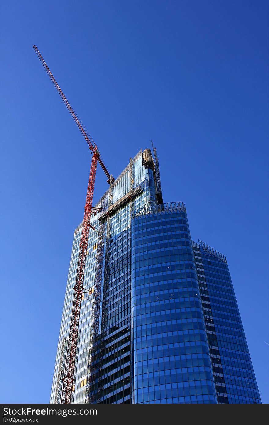 Modern building and hoist crane on the background of the blue sky. Modern building and hoist crane on the background of the blue sky