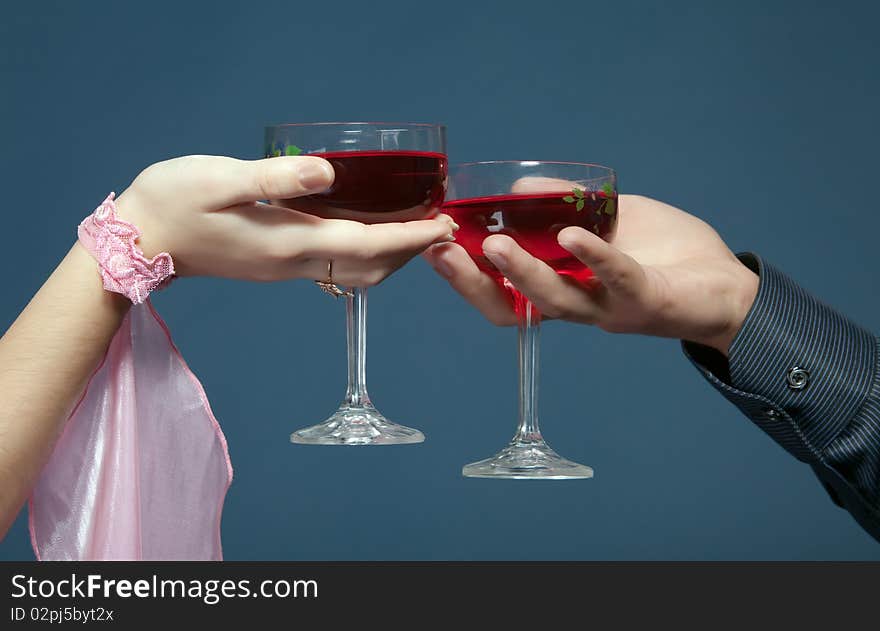 Two glasses with red wine in mans and female hands on dark blue background. Two glasses with red wine in mans and female hands on dark blue background