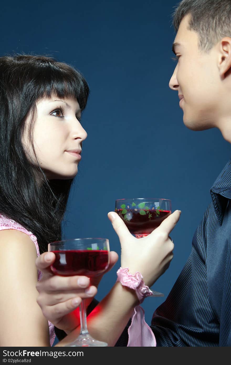 The girl and the guy with red wine glasses. They look against each other. The girl and the guy with red wine glasses. They look against each other