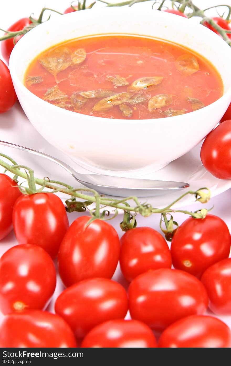 Tomato soup with basil leaves with fresh tomatoes around it and a spoon