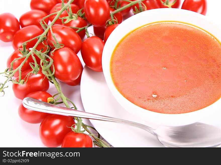 Tomato soup with fresh tomatoes around it and a spoon