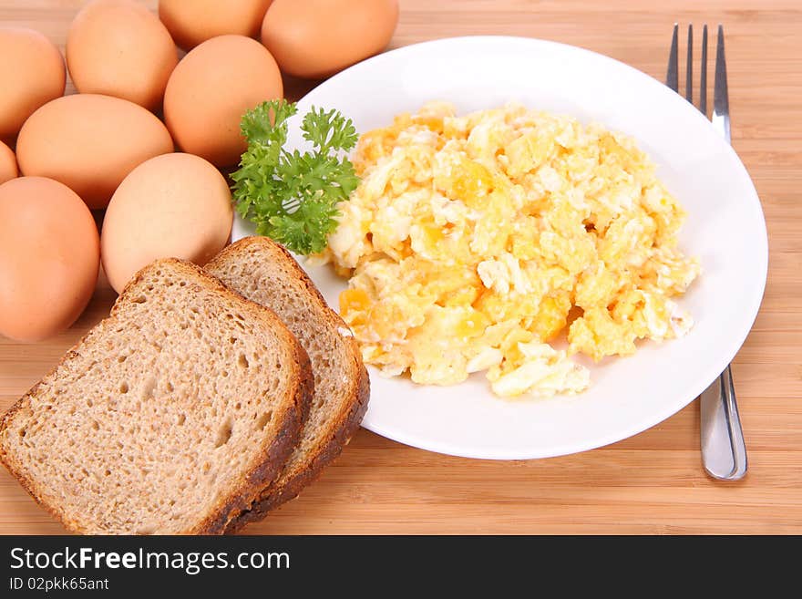 Scrambled eggs, some fresh eggs and wholemeal bread, and a fork, decorated with parsley