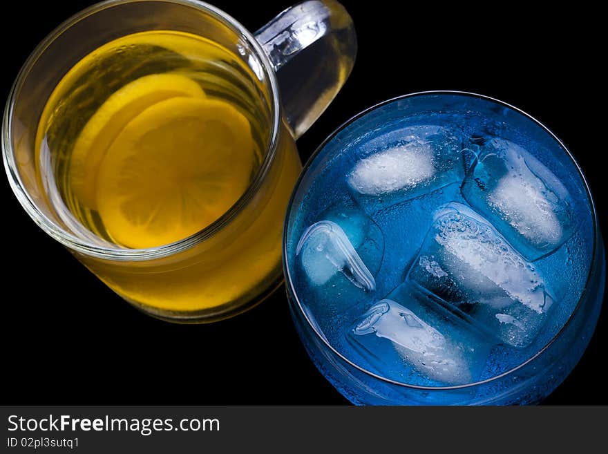 Ice tea and a blue drink with ice in a glass on a black background. Ice tea and a blue drink with ice in a glass on a black background