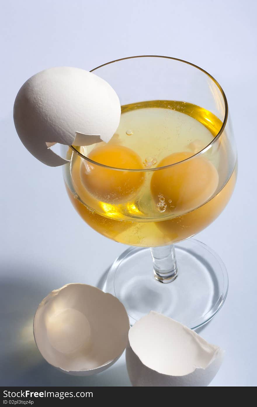 Two broken eggs in a glass and shells on a light background