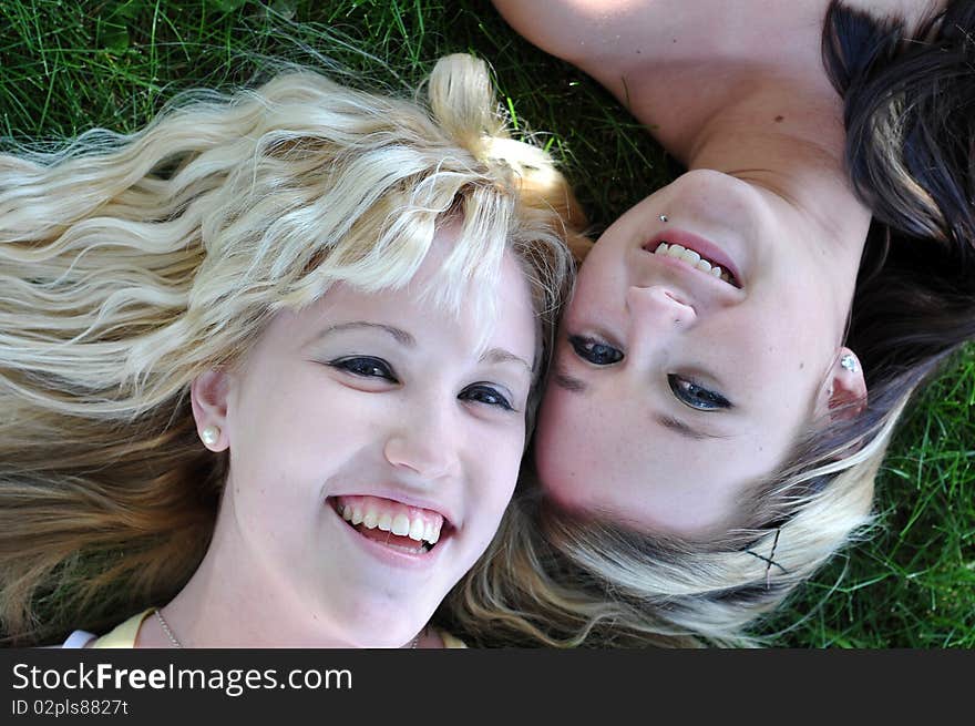 Close up of two lovely young teenage girls laying in grass smiling and laughing together. Close up of two lovely young teenage girls laying in grass smiling and laughing together.