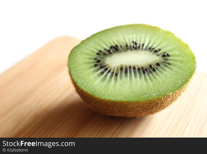 Half slice of a kiwi on wooden cutting board.