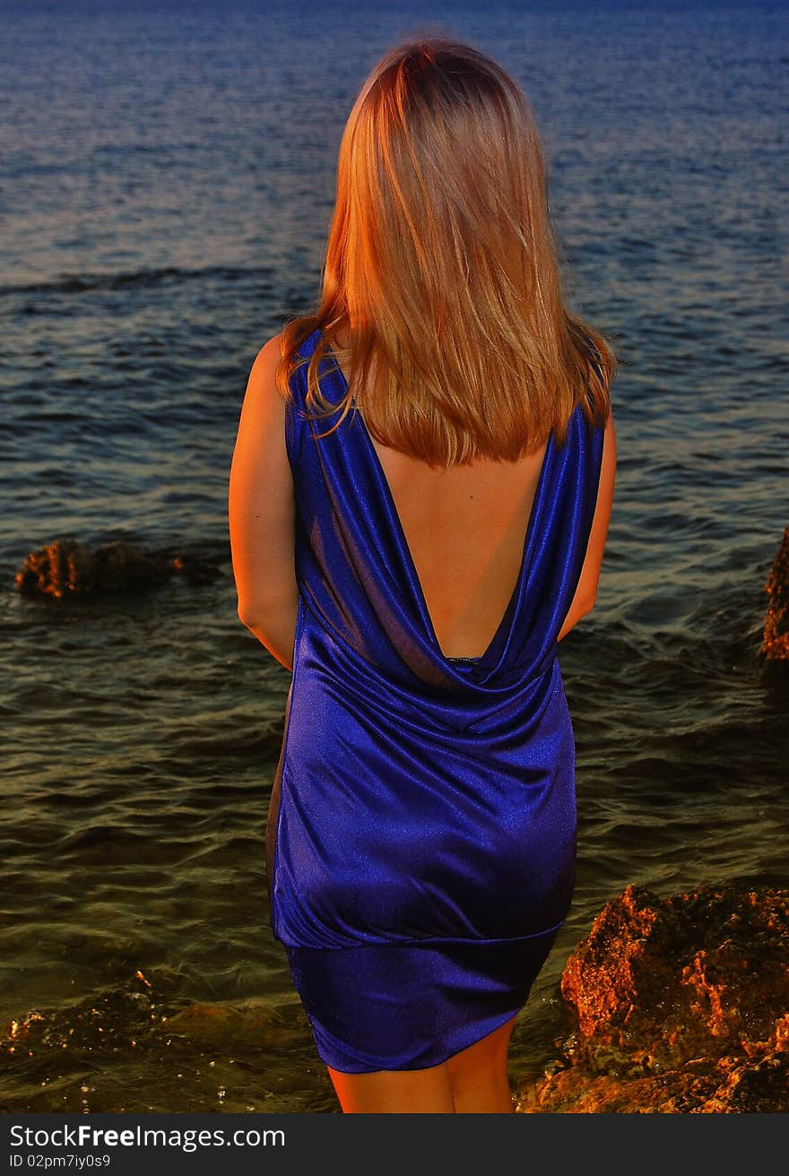 A thoughtful woman in violet dress standing on a small rock on beach. A thoughtful woman in violet dress standing on a small rock on beach