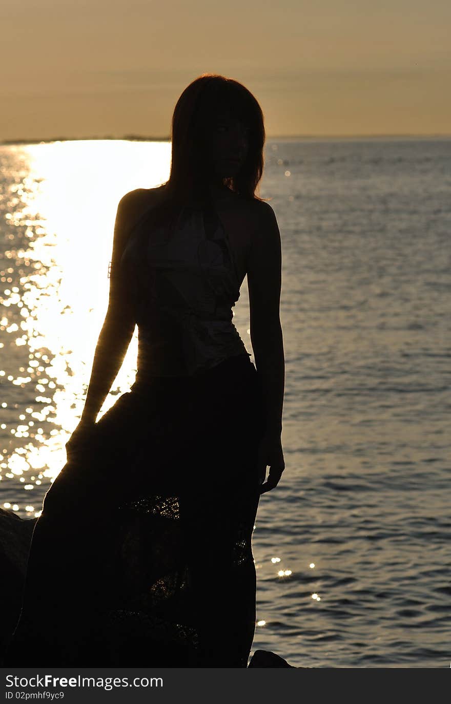 Silhouette of a young woman with slim figure against sea; warm lighting. Silhouette of a young woman with slim figure against sea; warm lighting