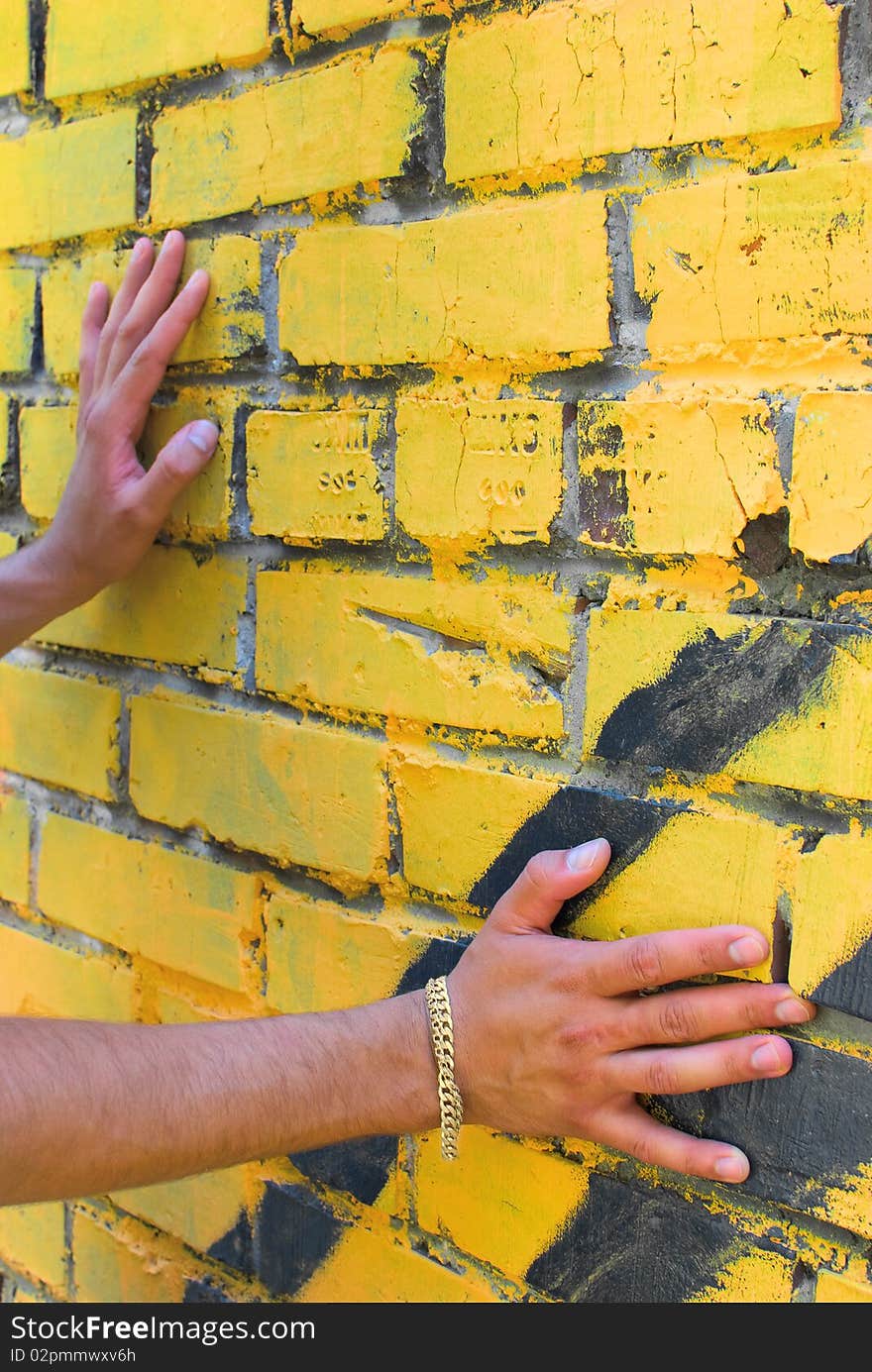 Hands of the young man are touching the wall. There is a yellow bracelet on right arm. Hands of the young man are touching the wall. There is a yellow bracelet on right arm.