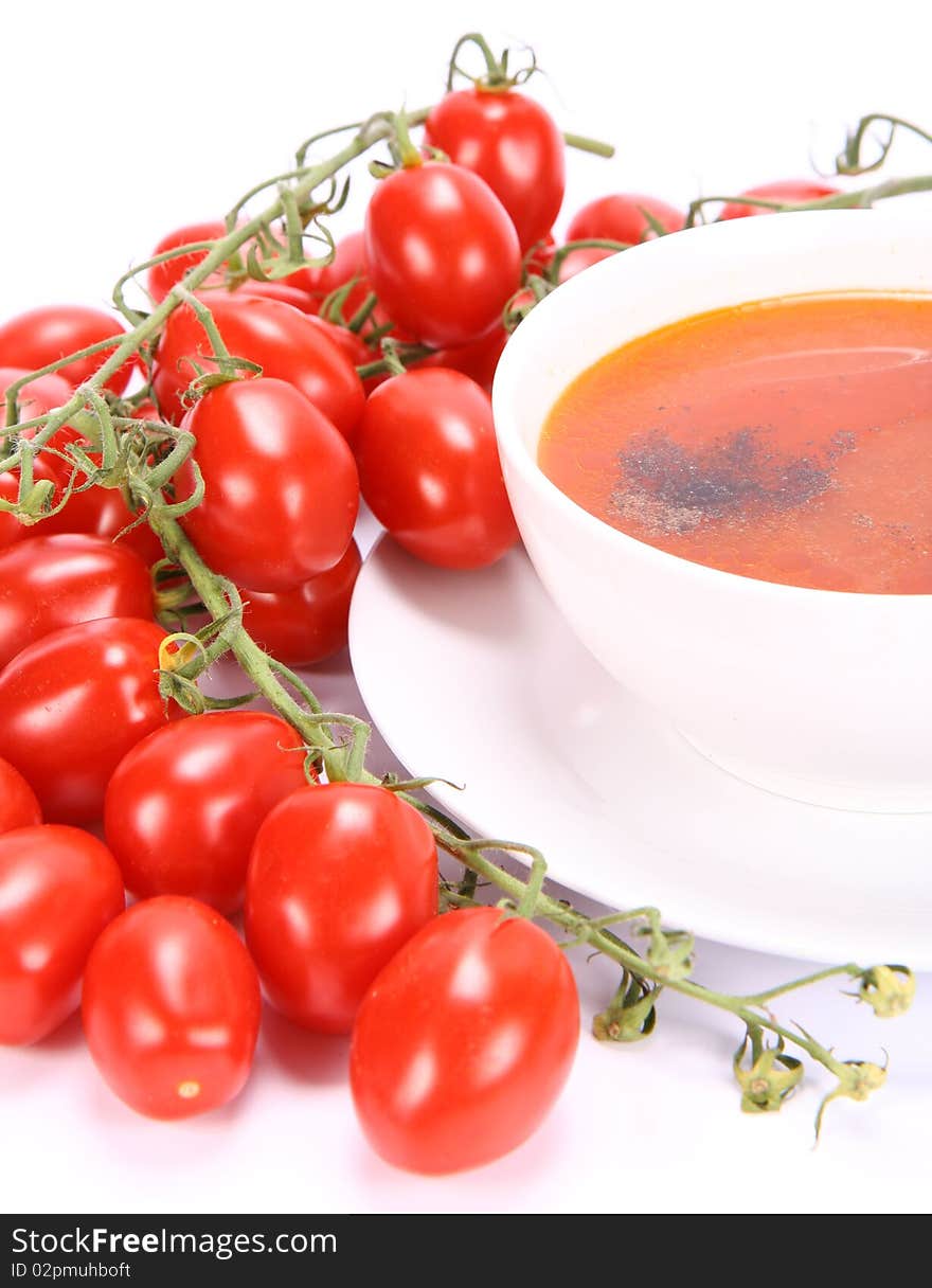 Tomato soup decorated with pepper with fresh tomatoes around it and a spoon