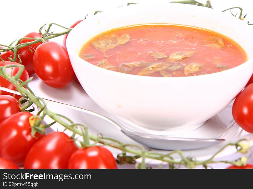 Tomato soup with basil leaves with fresh tomatoes around it and a spoon