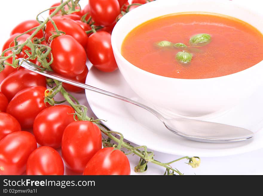 Tomato soup decorated with basil leaves with fresh tomatoes around it and a spoon