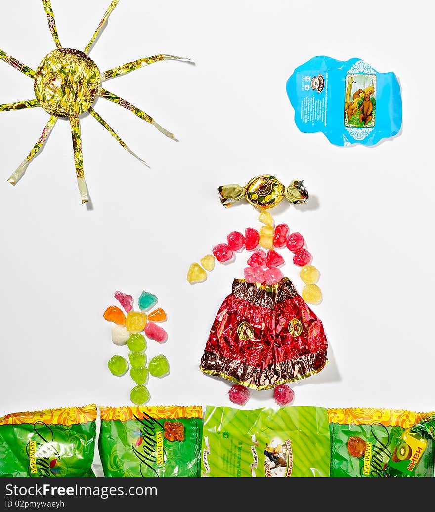 The picture made of candy wrappers and fruit drops shows the landscape with a girl and a flower. The picture made of candy wrappers and fruit drops shows the landscape with a girl and a flower