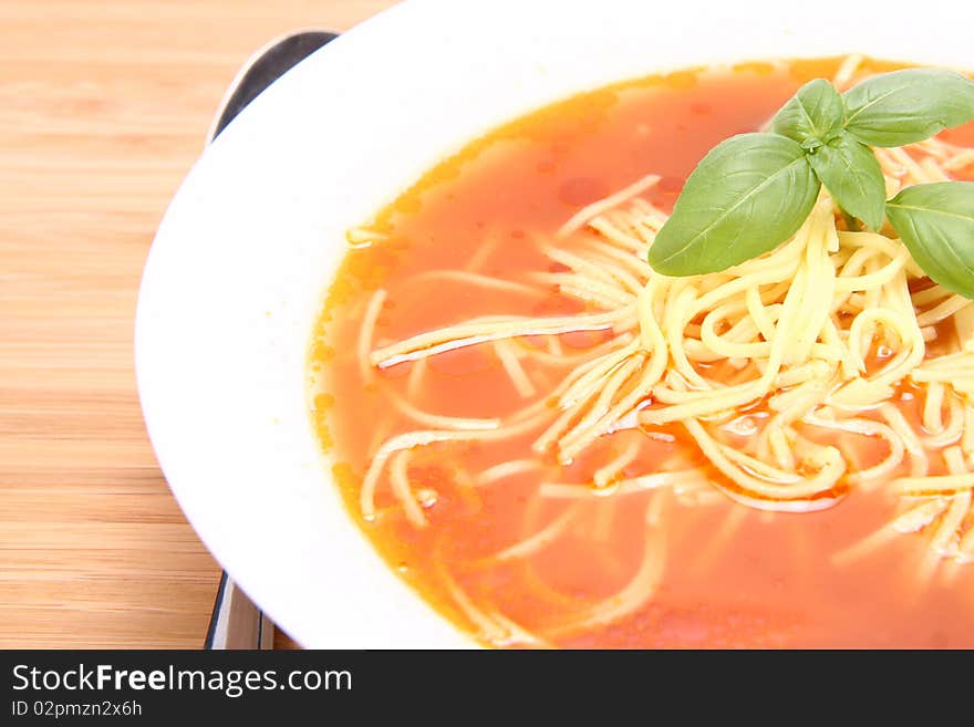 Tomato soup decorated with basil leaves with a spoon on wooden background