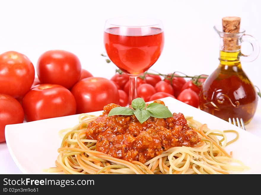 Colorful spaghetti bolognese on a plate, some fresh tomatoes, olive oil and a glass of pink wine