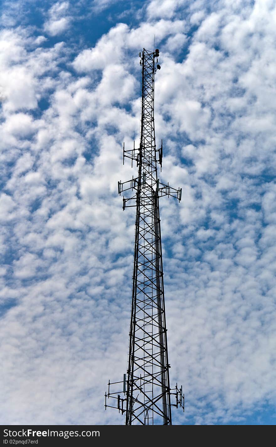 A communication tower against at fluffy cloud filled blue sky.