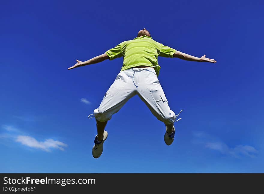 Jumping up guy in a green shirt against blue sky.