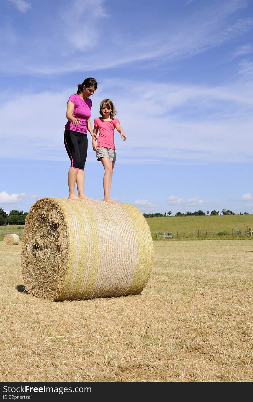 Caucasian mother and daughter playing with hay bales in summer season, blue sky in background. Caucasian mother and daughter playing with hay bales in summer season, blue sky in background