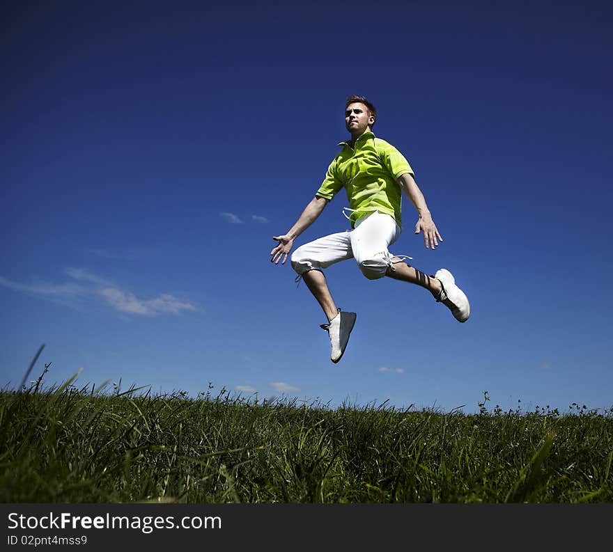 Jumping up guy in a green shirt against blue sky.