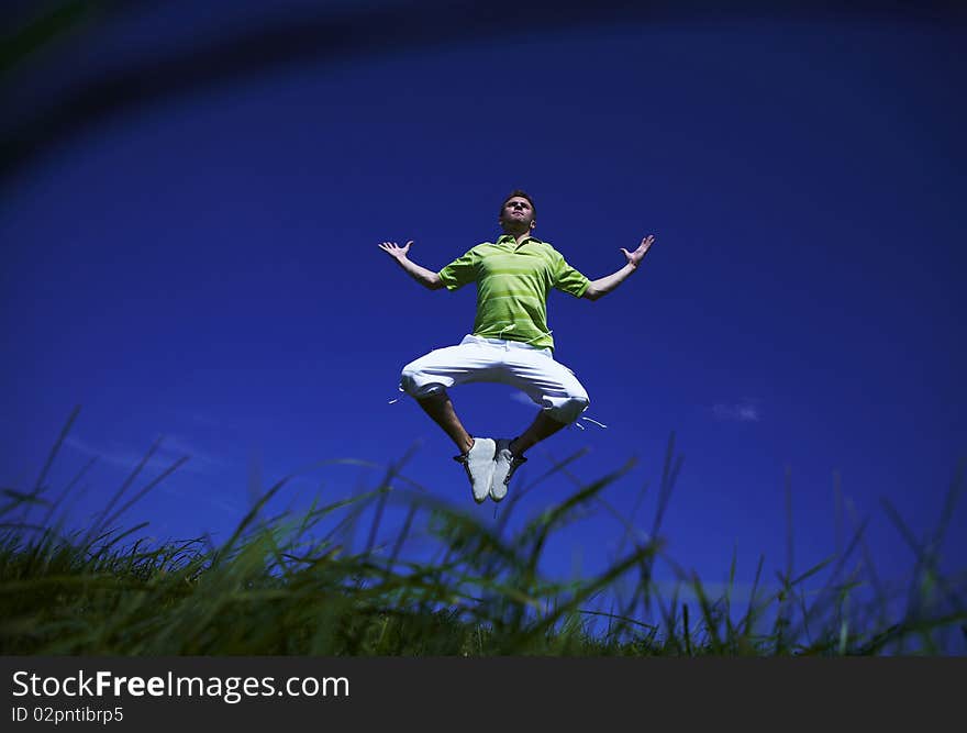 Jumping up guy in a green shirt against blue sky.