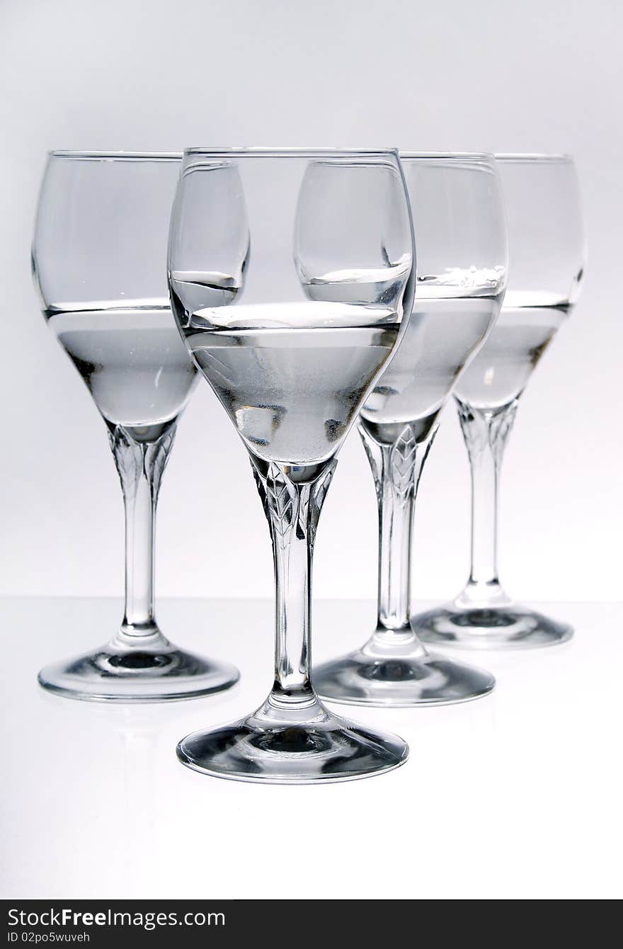 Four wine glasses half full of a clear liquid