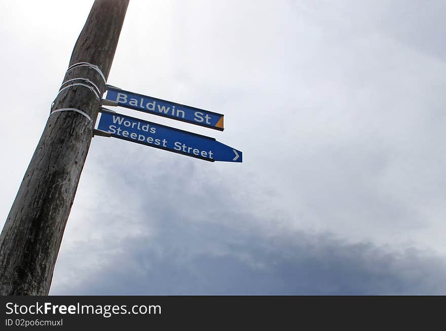 Blue street sign attached to a wooden pole. Cloudy sky in the background. Worlds Steepest Street. Metaphor for challenges faced in business, etc...