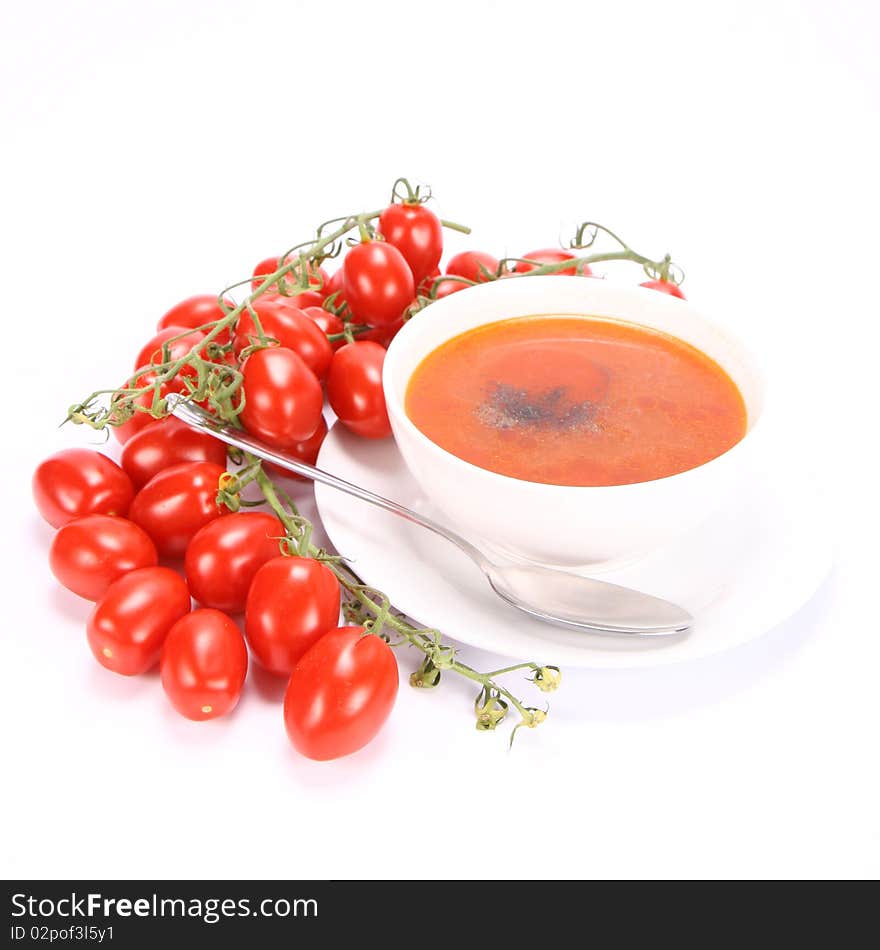 Tomato soup decorated with pepper with fresh tomatoes around it and a spoon