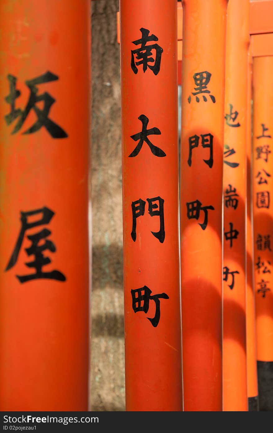 Japanese script on the bright orange arches leading to a temple.