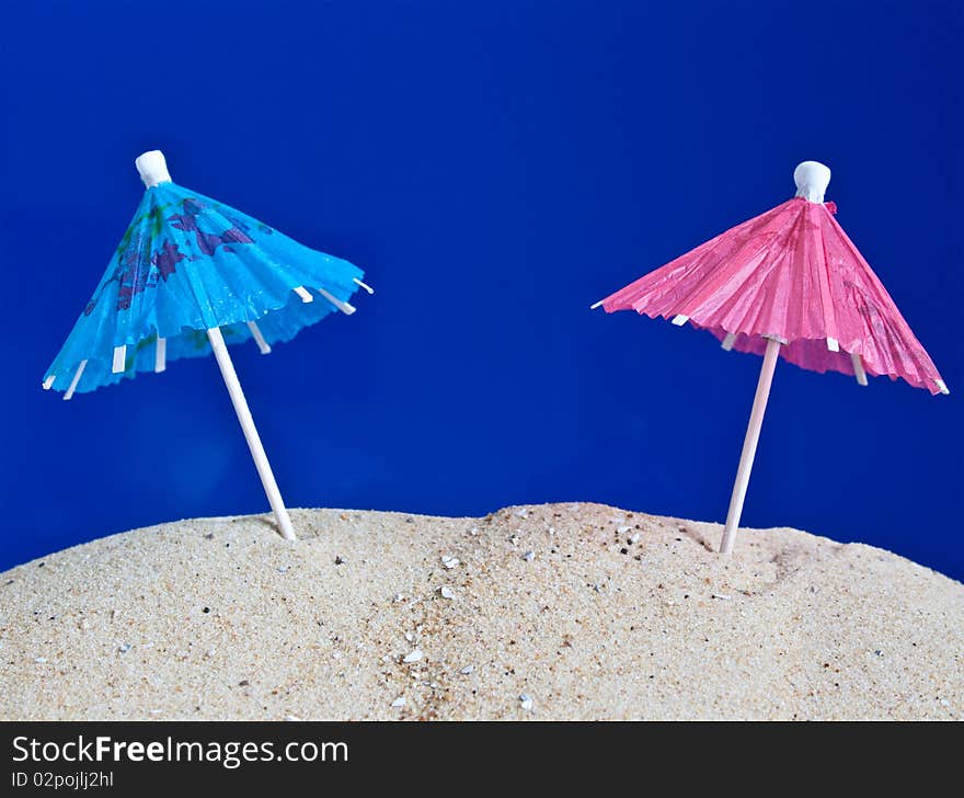 Blue and pink cocktail umbrellas standing in the sand. Blue and pink cocktail umbrellas standing in the sand