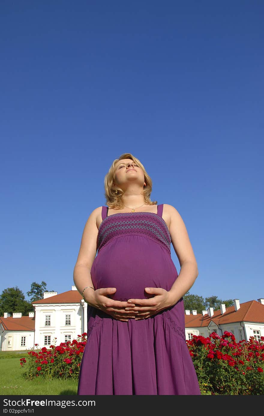 Pregnant woman with hands on the belly in the garden in front of the palace