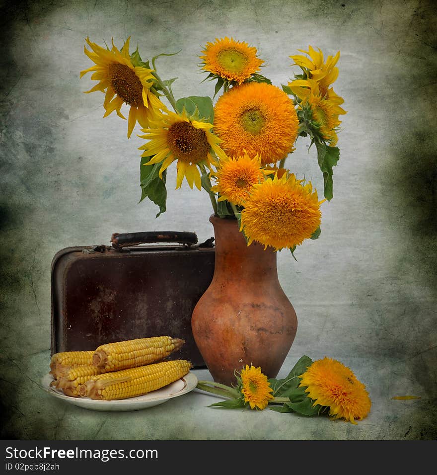 The bouquet of sunflowers stands in a jug, alongside old suitcase and boiled corn. The bouquet of sunflowers stands in a jug, alongside old suitcase and boiled corn