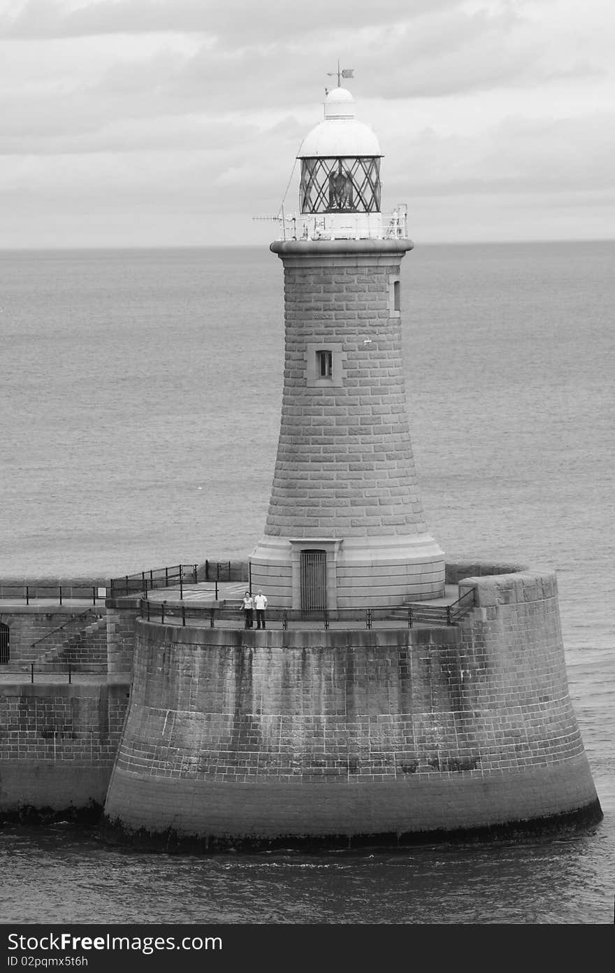 A shot of a lighthouse taken when sailing out of the Newcastle harbor. The horizon lines up perfectly with the roof of the house. A couple is standing at the base. A shot of a lighthouse taken when sailing out of the Newcastle harbor. The horizon lines up perfectly with the roof of the house. A couple is standing at the base.