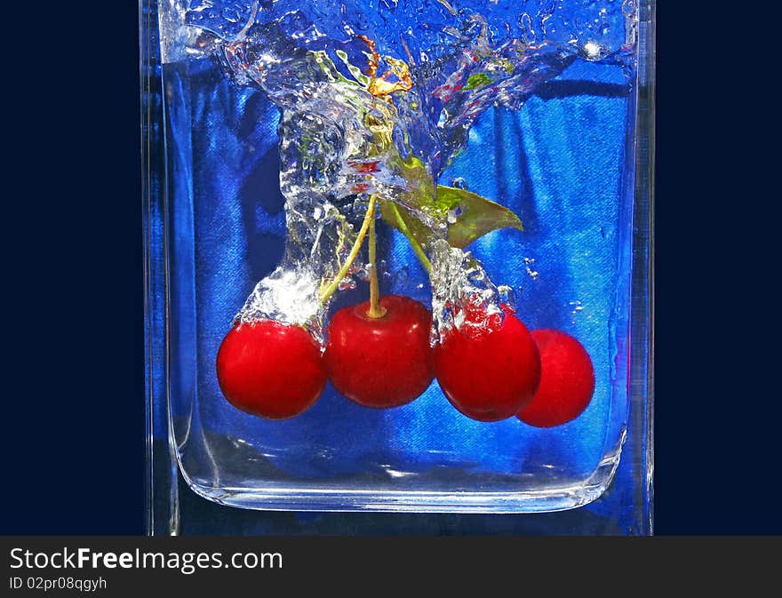 Ripe cherries fall in a glass with water