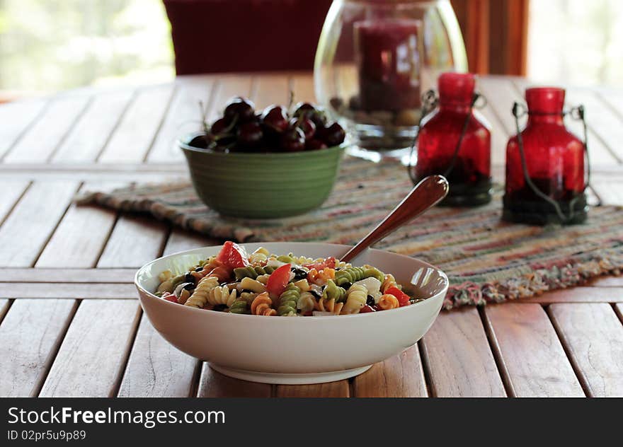 A teak wood table with fresh summer cherries and pasta salad. A teak wood table with fresh summer cherries and pasta salad.